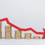 Seta vermelha descendo sobre moedas, representando os bancos com taxas de juros mais baixas​.