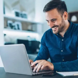 Imagem de um homem sorridente usando notebook, para ilustrar um texto sobre como se tornar correspondente bancário.