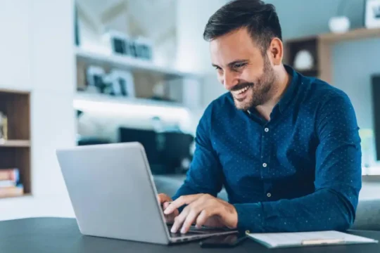 Imagem de um homem sorridente usando notebook, para ilustrar um texto sobre como se tornar correspondente bancário.