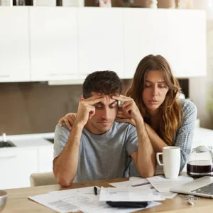 Um casal olha preocupado para as faturas que estão sobre a mesa, ilustrando um artigo da BKOpen sobre como conseguir empréstimo negativado e score baixo.