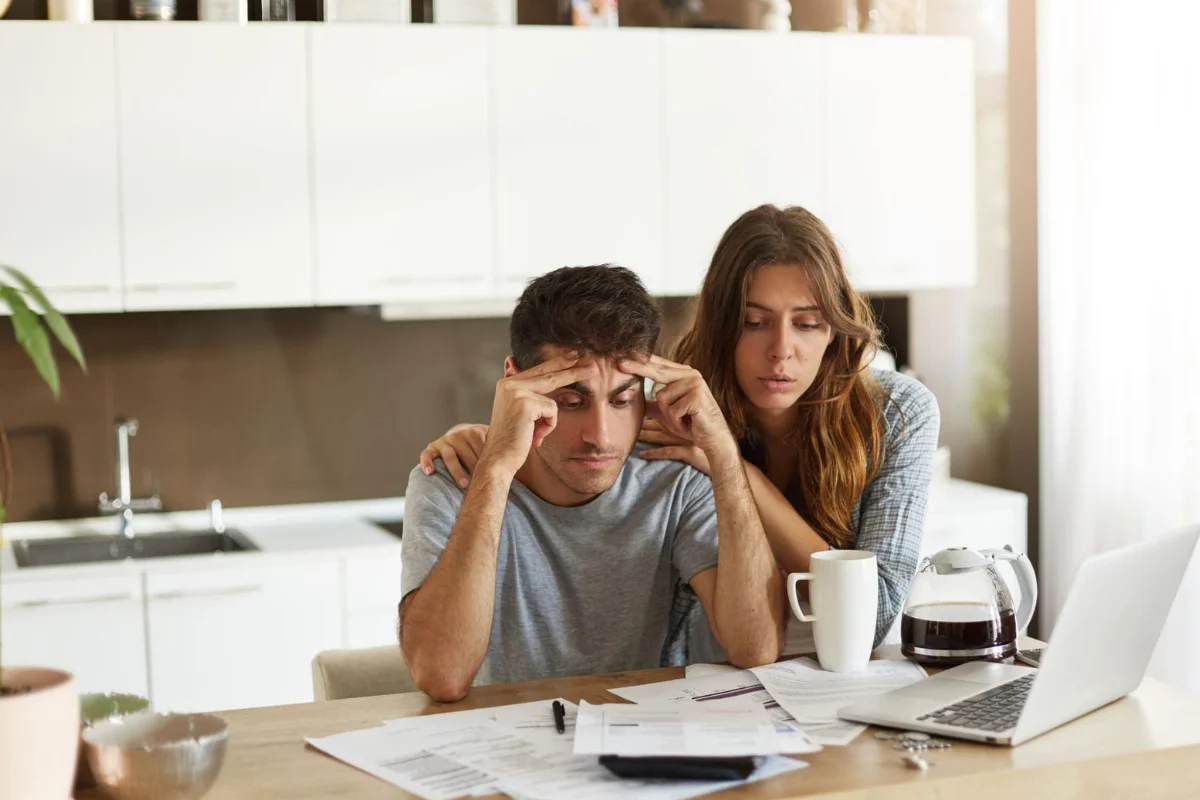 Um casal olha preocupado para as faturas que estão sobre a mesa, ilustrando um artigo da BKOpen sobre como conseguir empréstimo negativado e score baixo.