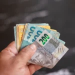 Mão segurando cédulas de real brasileiro em diferentes valores, representando um artigo da BKOpen sobre como funciona o empréstimo consignado para CLT.