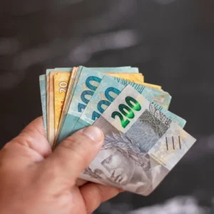 Mão segurando cédulas de real brasileiro em diferentes valores, representando um artigo da BKOpen sobre como funciona o empréstimo consignado para CLT.