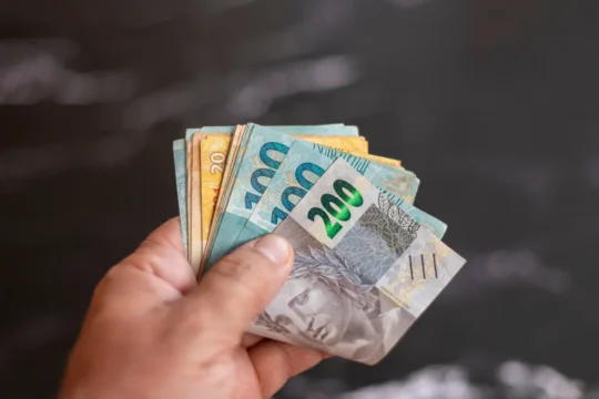 Mão segurando cédulas de real brasileiro em diferentes valores, representando um artigo da BKOpen sobre como funciona o empréstimo consignado para CLT.