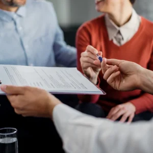 Duas pessoas assinam um contrato com um consultor financeiro, ilustrando um artigo da BKOpen sobre o que é preciso para fazer um consórcio.
