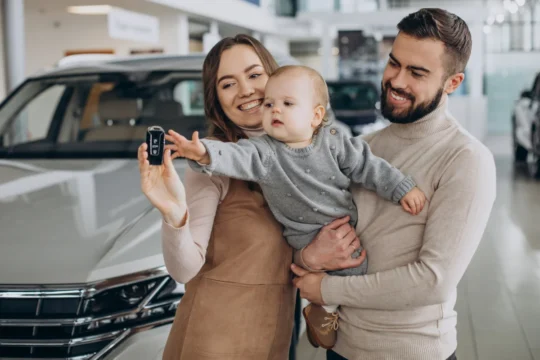 Família feliz segurando chave de carro novo em concessionária, ilustrando um artigo da BKOpen sobre quanto custa um seguro de carro.