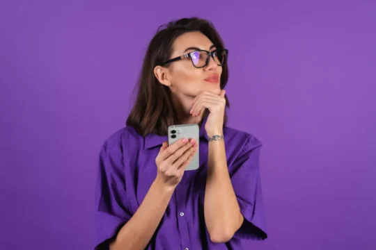 Mulher pensativa segurando smartphone em fundo roxo, ilustrando um artigo da BK Open sobre bancos tradicionais.