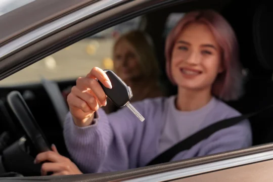 Mulher sorridente segurando chave de carro dentro do veículo com passageira ao fundo, ilustrando um artigo da BKOpen sobre qual melhor consórcio do Brasil.