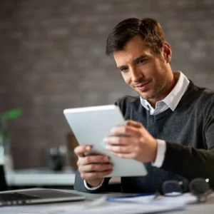Homem usando tablet em escritório de paredes cinzas, ilustrando um conteúdo da BKOpen sobre personal banker.